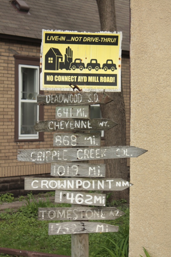 The yellow and black sign is in protest of a proposal to directly connect the nearby Ayd Mill Road to I-94. The distance markers below it point toward various cities and towns to the west. Cripple Creek is a small Colorado town near the base of Pike’s Peak made famous in a 1969 song by the band “The Band”.)
