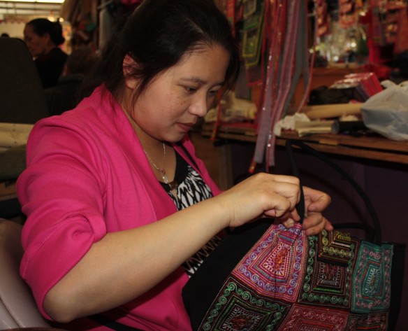 In a booth at the Market a woman stitches a traditional Hmong outfit. 