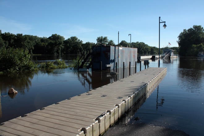 Water laps at the temporary pier, installed presumably to allow boaters access while the permanent piers were under water. Notice the street light, two buildings in the background and the bushes on the left are all surrounded by water.
