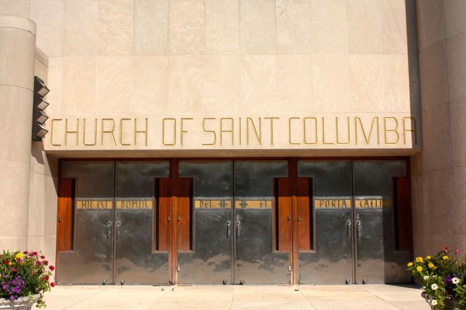 The steel doors and above them, the stunning gold lettering are strongly set off by the white stone building