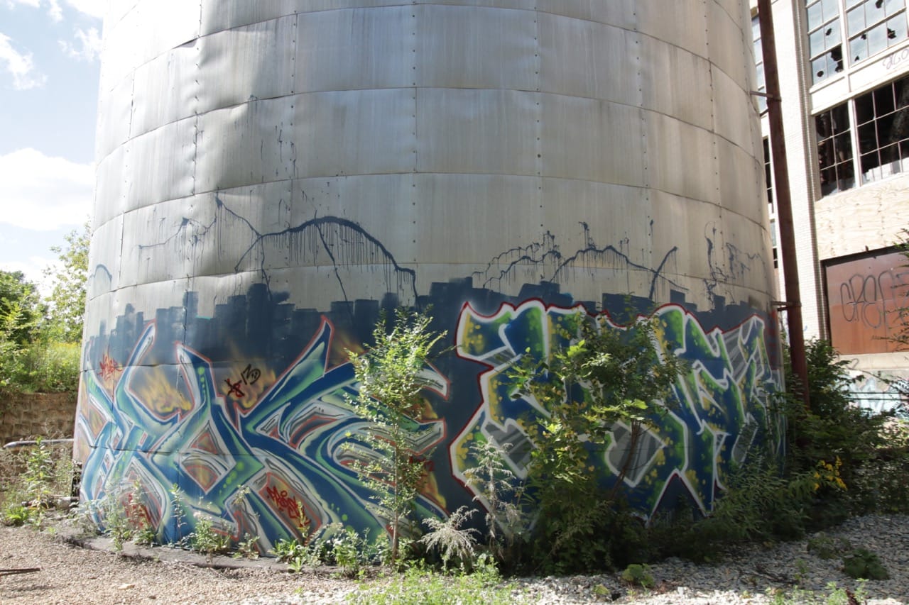 A storage tank next to the steam plant wears an elaborately spray painted design. 